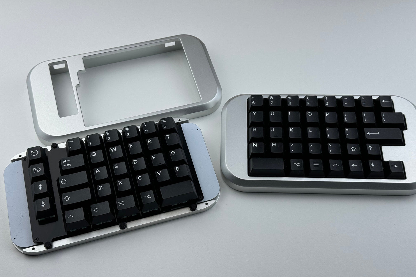 Closeup view of an opened silver Hall effect split keyboard with black keycaps, ortholinear layout for gaming