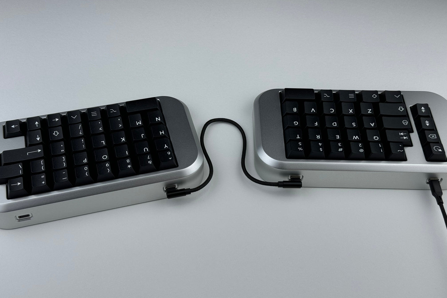 Back view of a silver Hall effect split wired keyboard with black keycaps, ortholinear layout for gaming