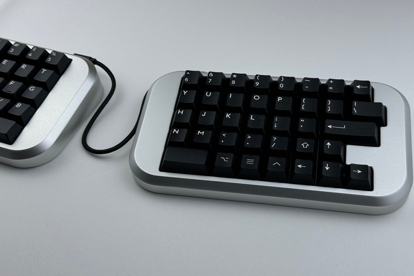 Closeup view of a silver Hall effect split wired keyboard with black keycaps, ortholinear layout for gaming